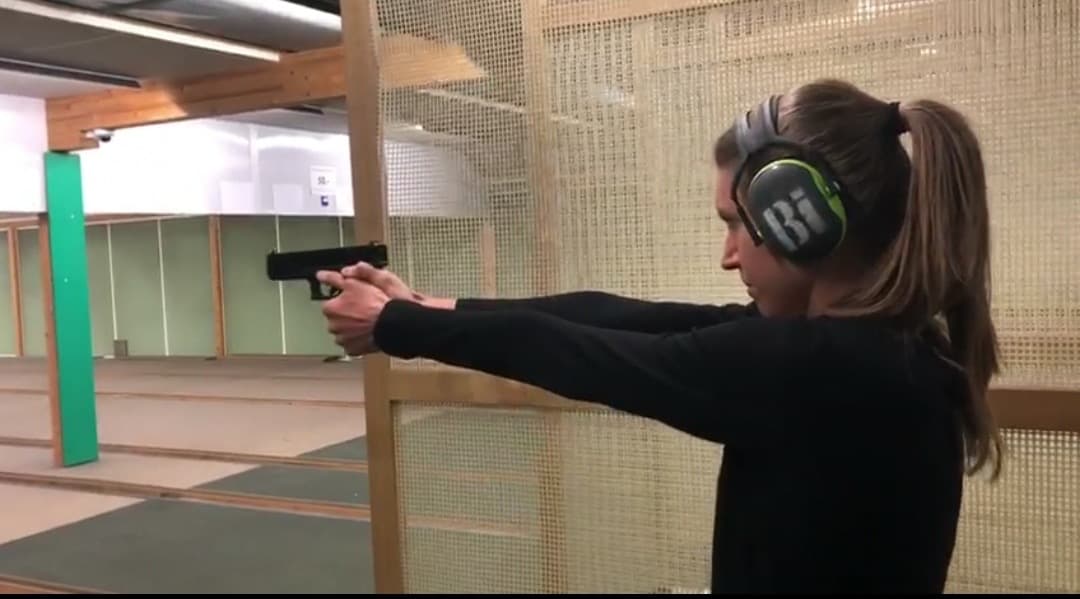 Schützin mit Gehörschutz zielt mit einer Pistole